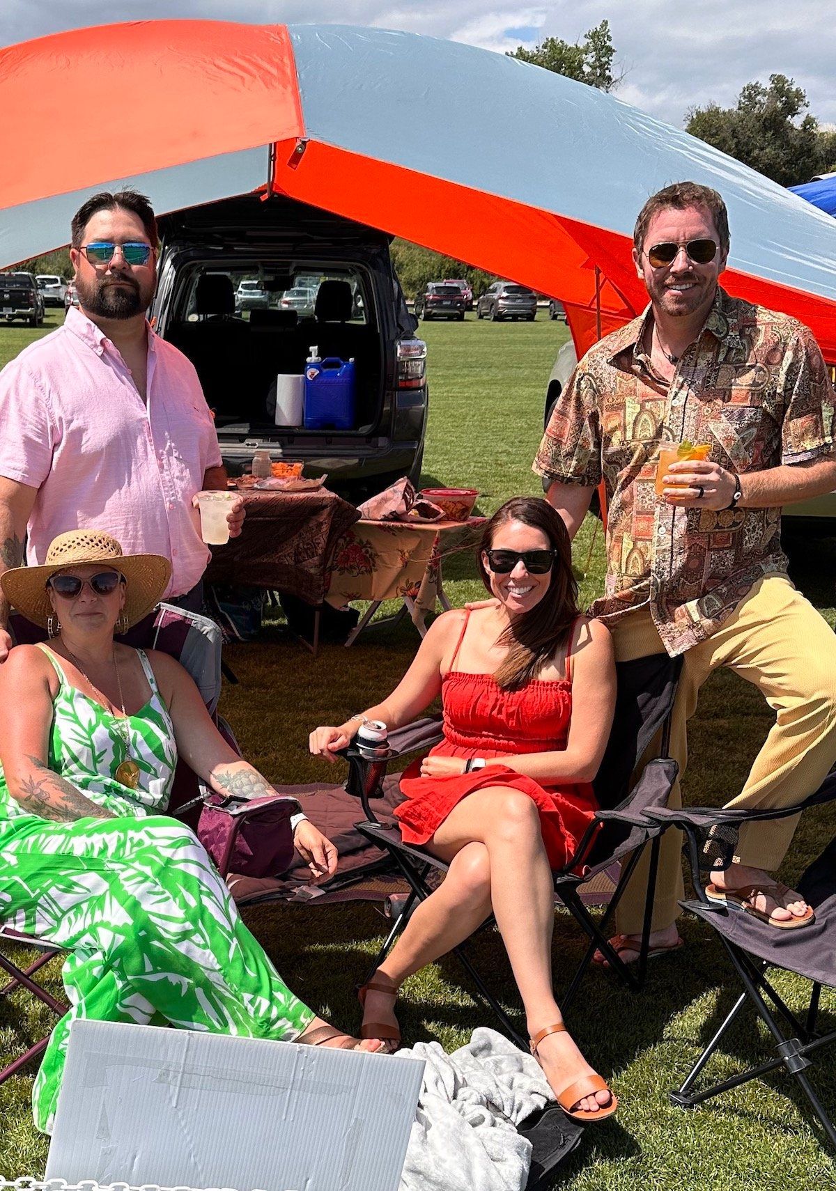 A group of people are sitting under an umbrella in a field.