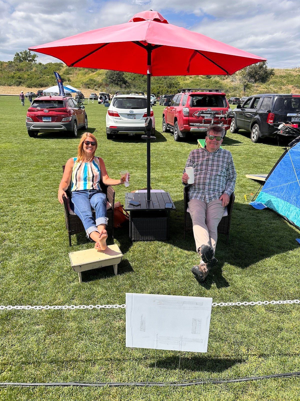 Two people are sitting under an umbrella in a field.