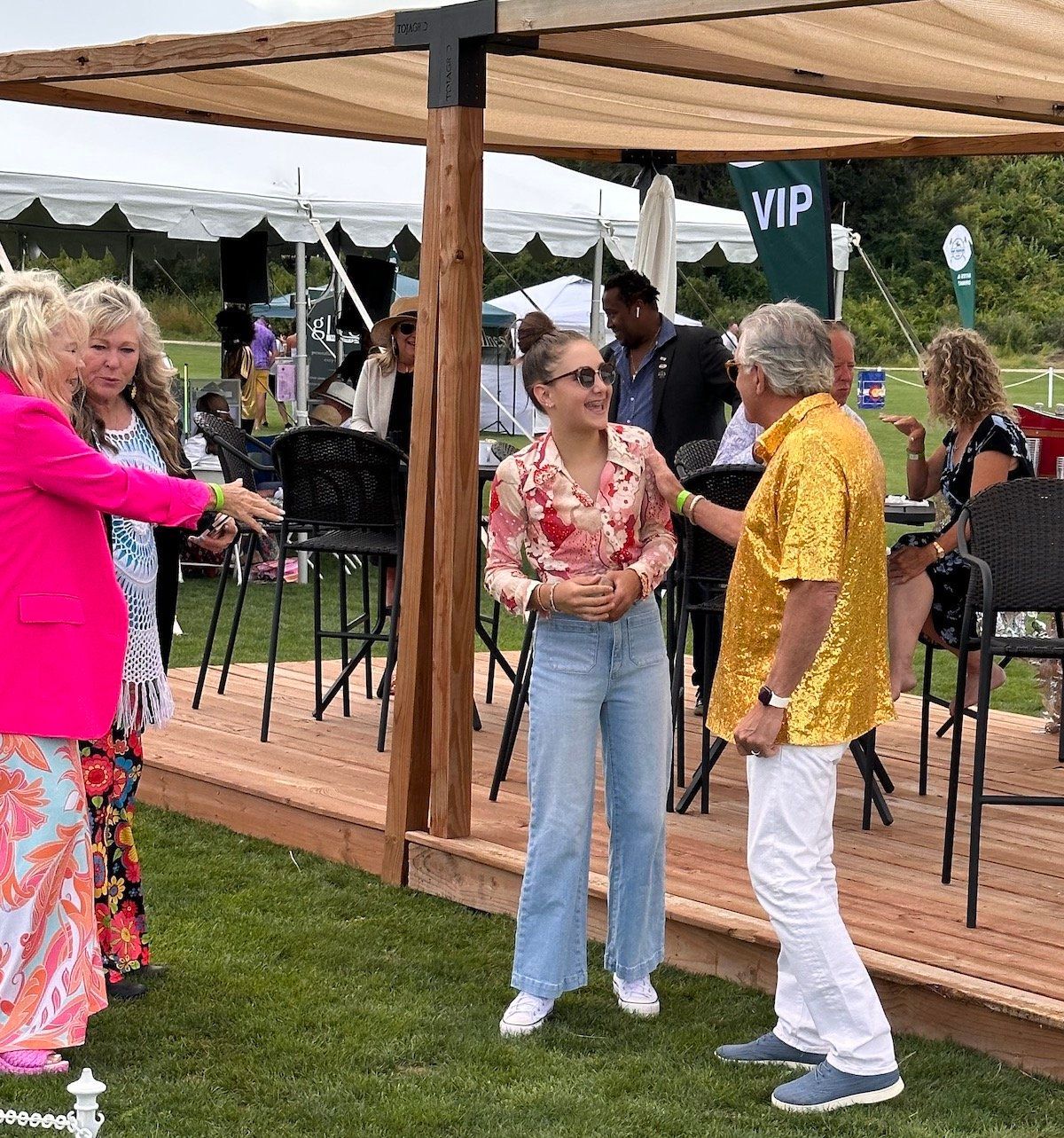 A group of people are standing on a wooden deck talking to each other.