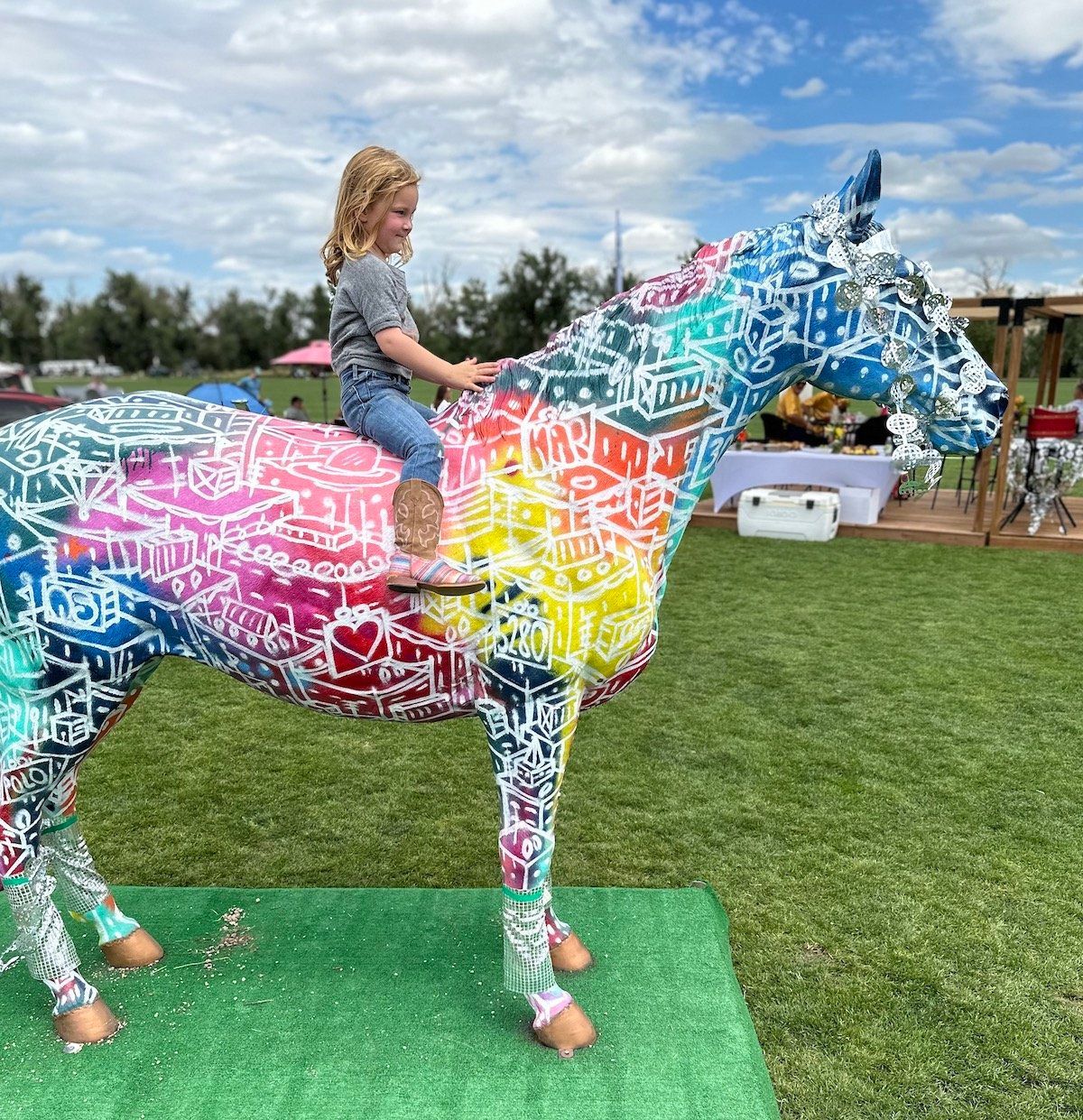 A little girl is sitting on the back of a colorful horse statue.