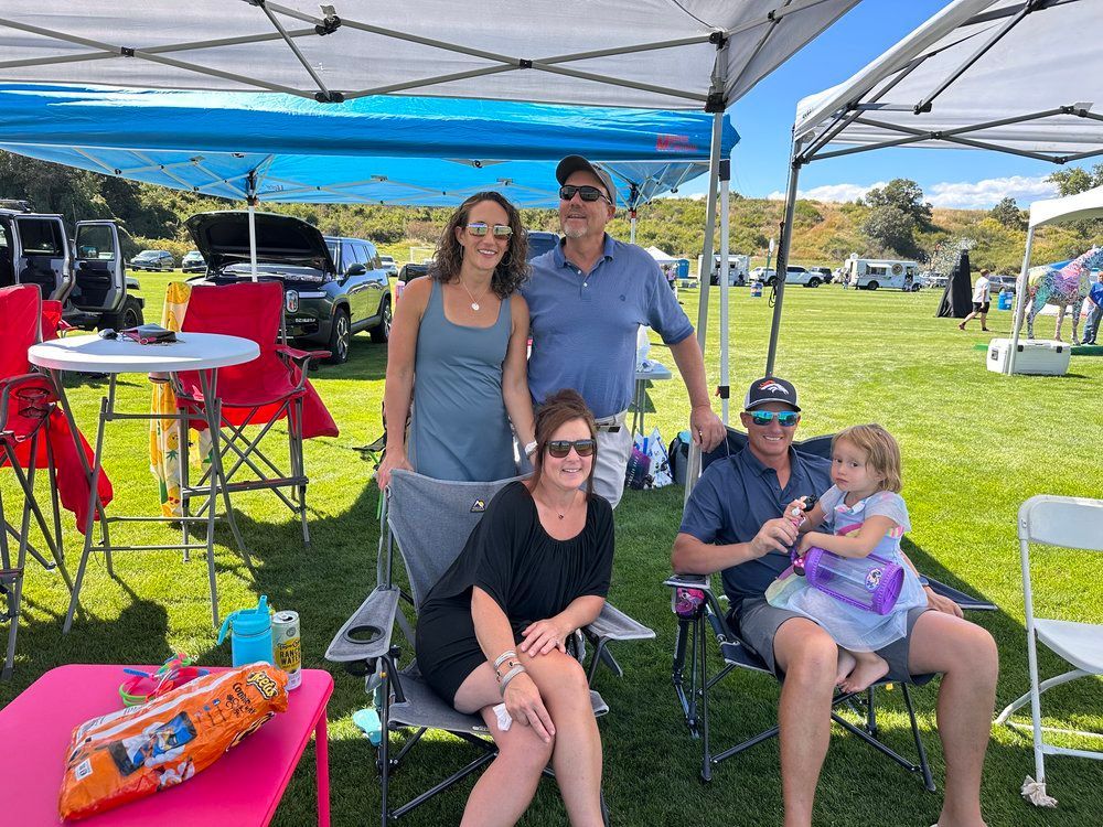 A group of people are sitting under a tent in a field.