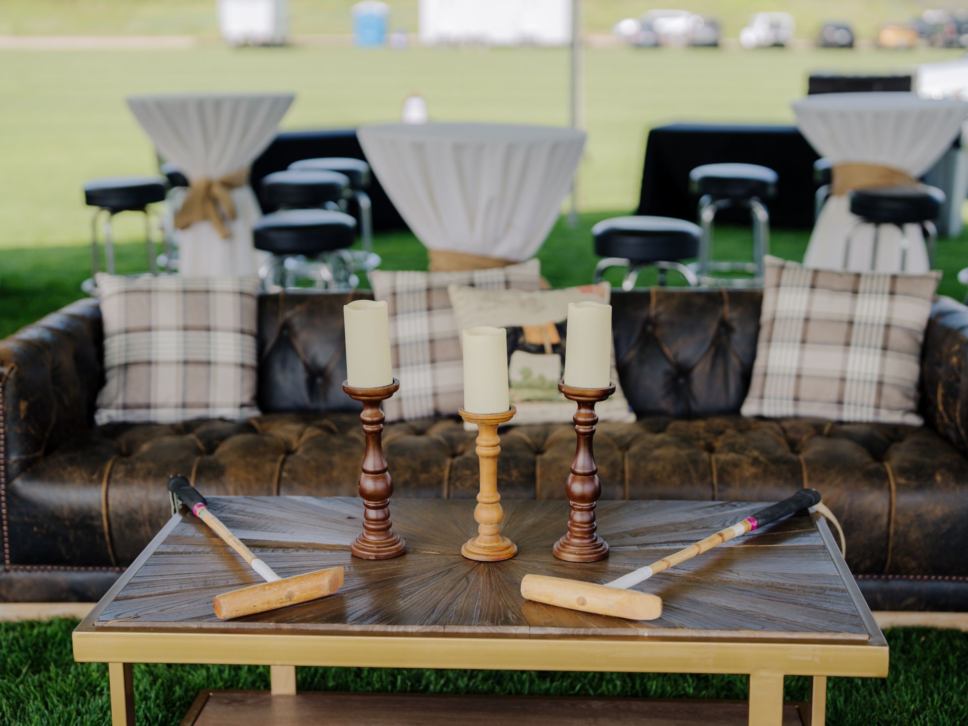 Outdoor event seating with leather sofa, cocktail tables, candles, and polo mallets.