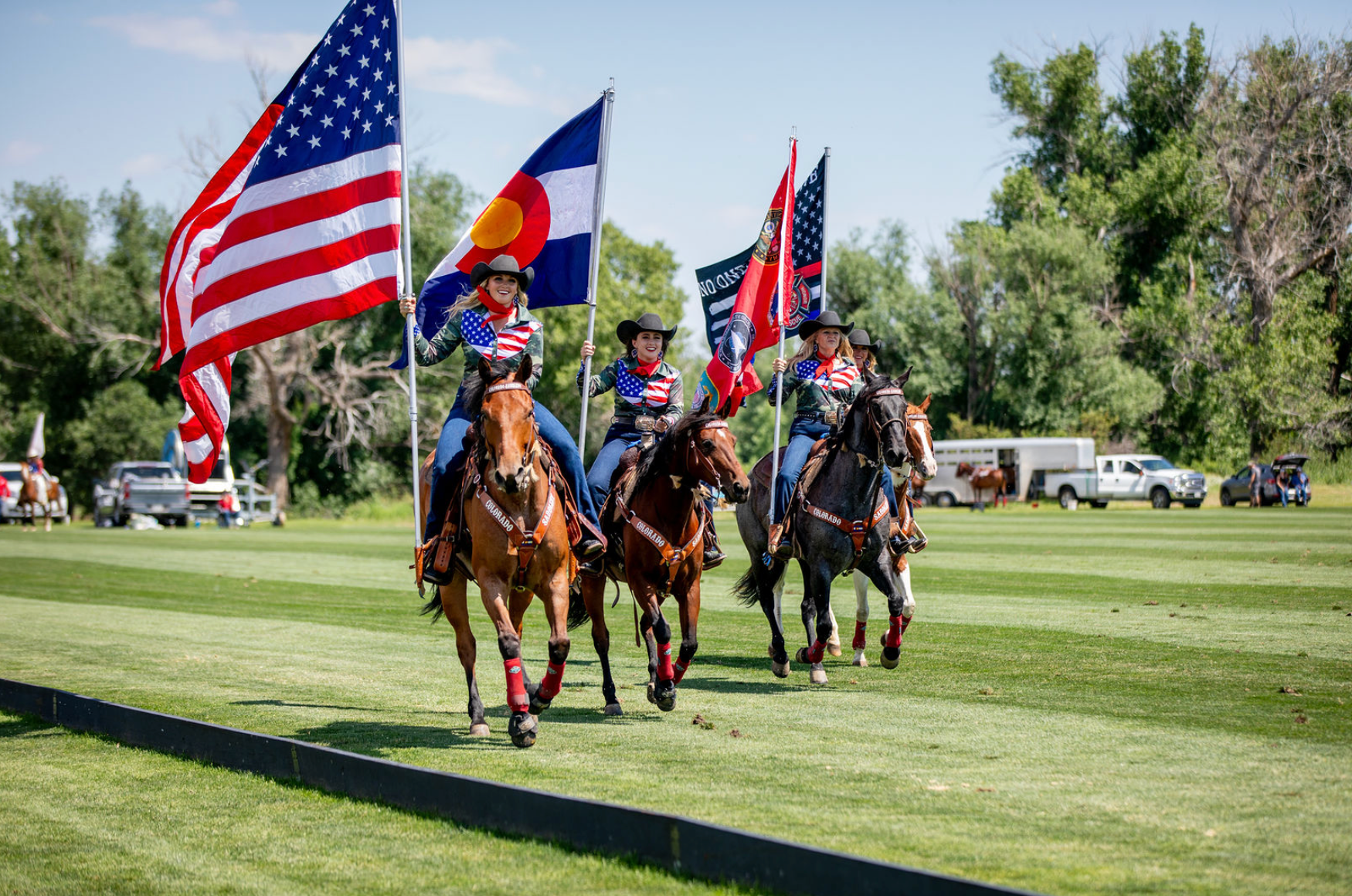 A group of people are riding horses in a field while holding flags.