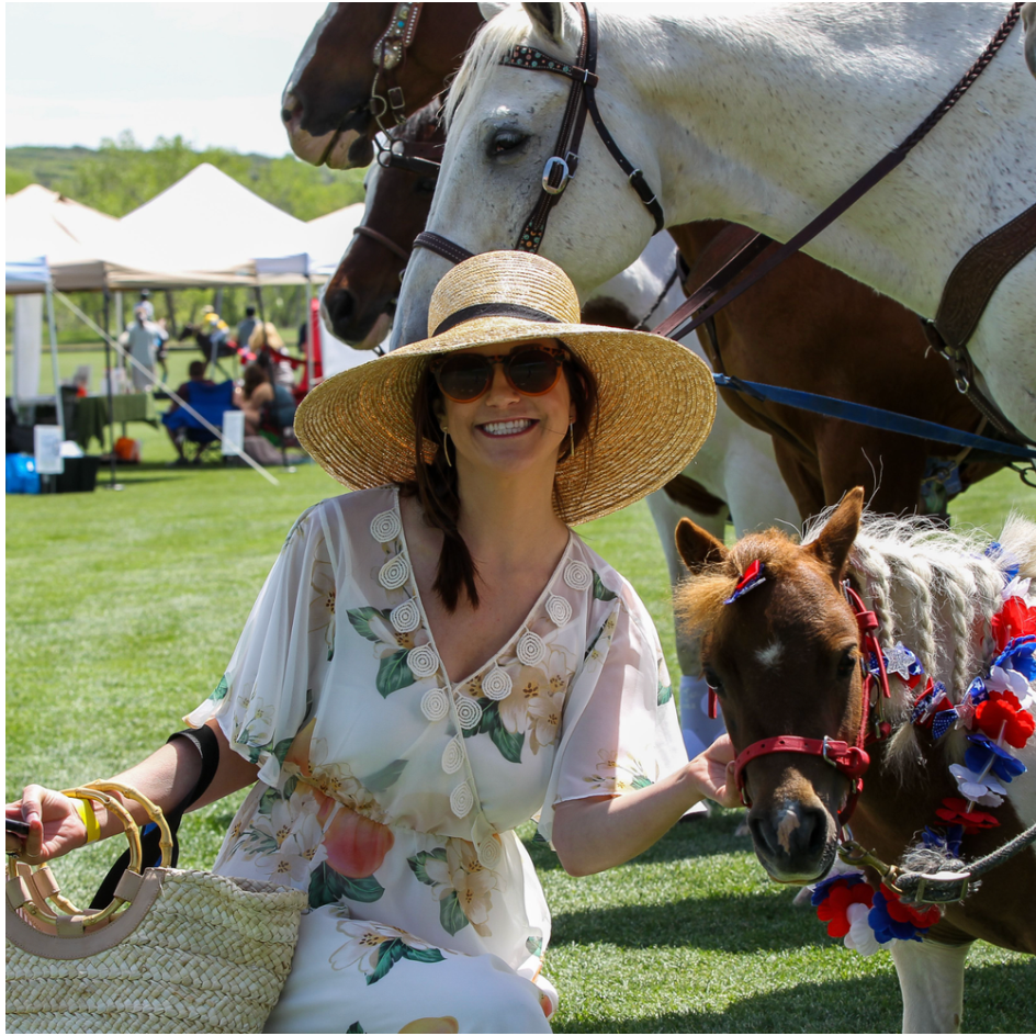 A woman wearing a straw hat stands next to a horse