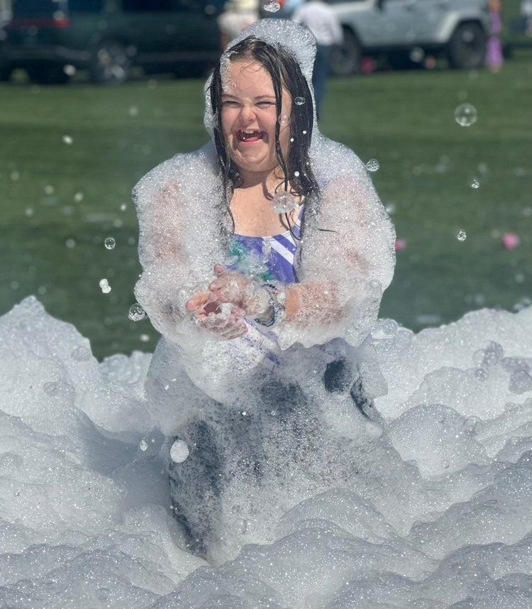 A little girl is sitting in a pile of soap bubbles.