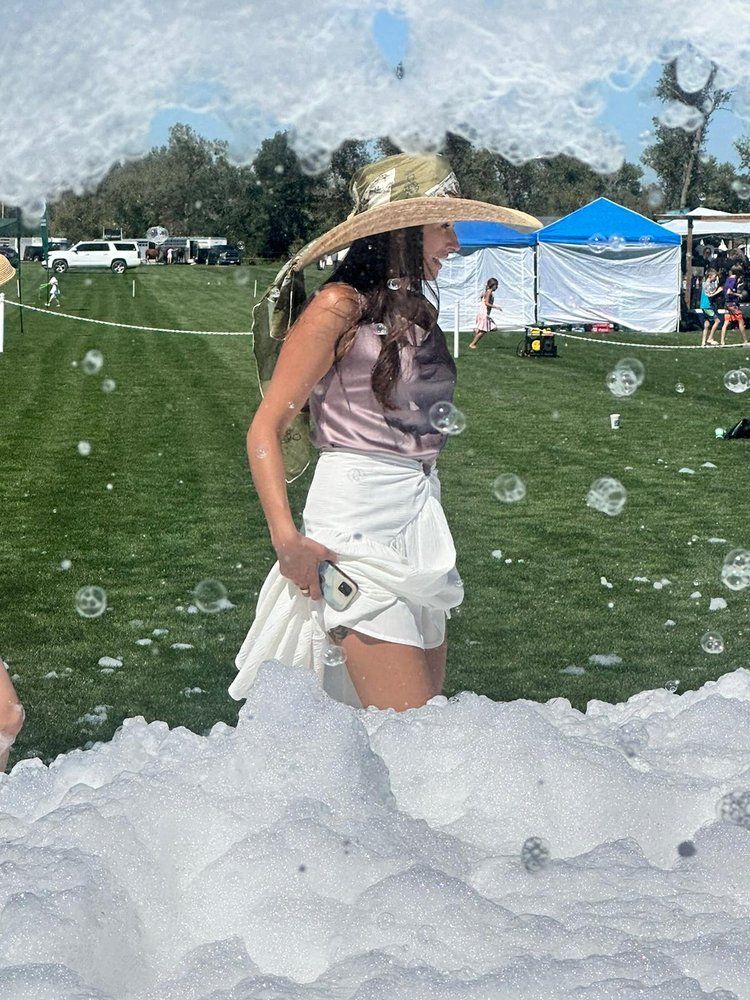 A woman in a hat is standing in a field of soap bubbles.