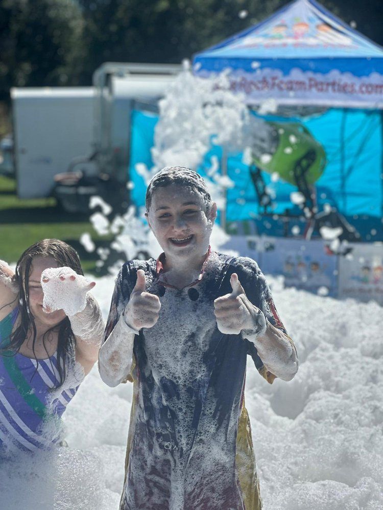 A boy and a girl are covered in foam and giving a thumbs up.