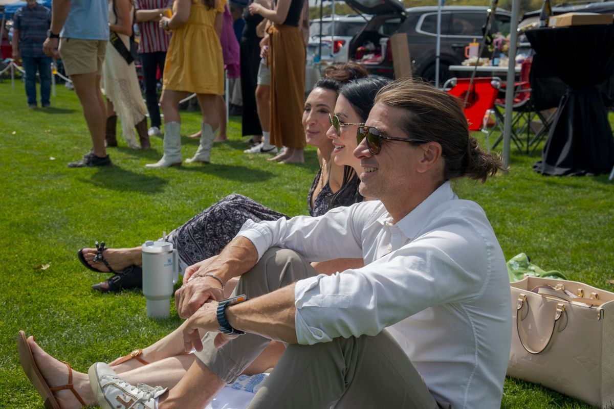 People sit on grass, enjoying a sunny outdoor event.