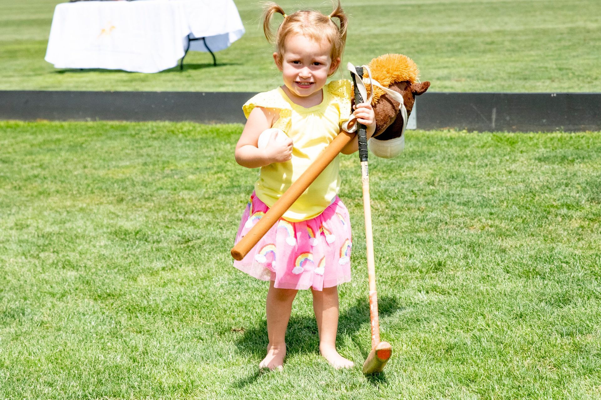 A little girl is holding a stick and a stuffed horse.