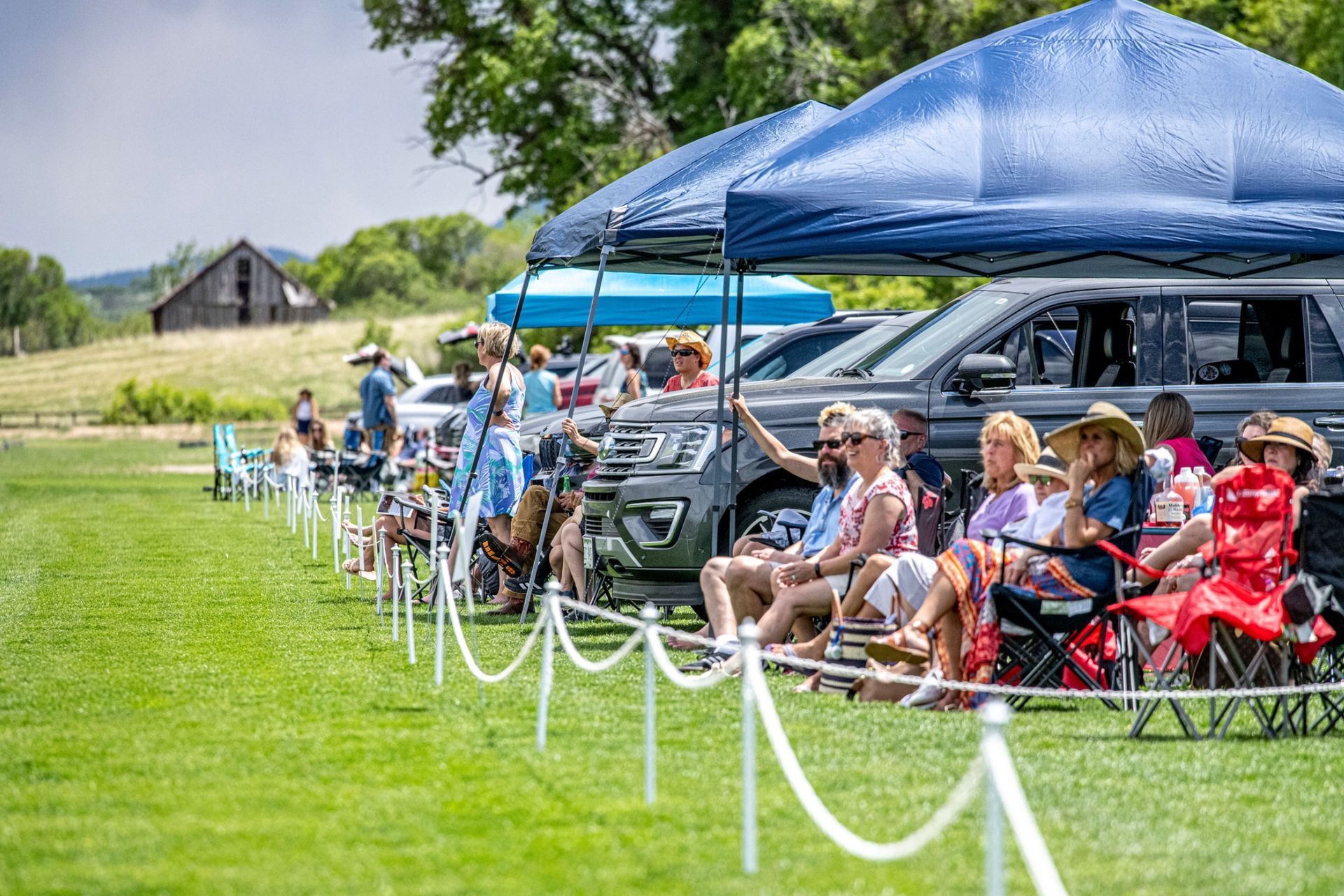 A group of people are sitting under tents in a field.