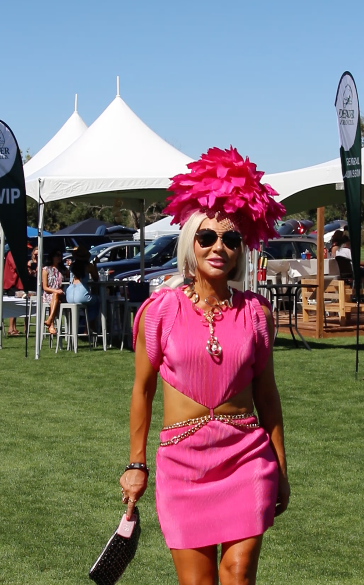 A woman in a pink dress and pink hat is walking in a field.
