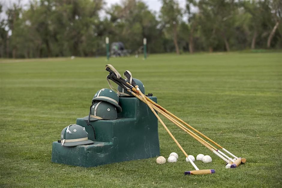 Polo equipment on a green field. Helmets and mallets rest on a green stand beside white balls.