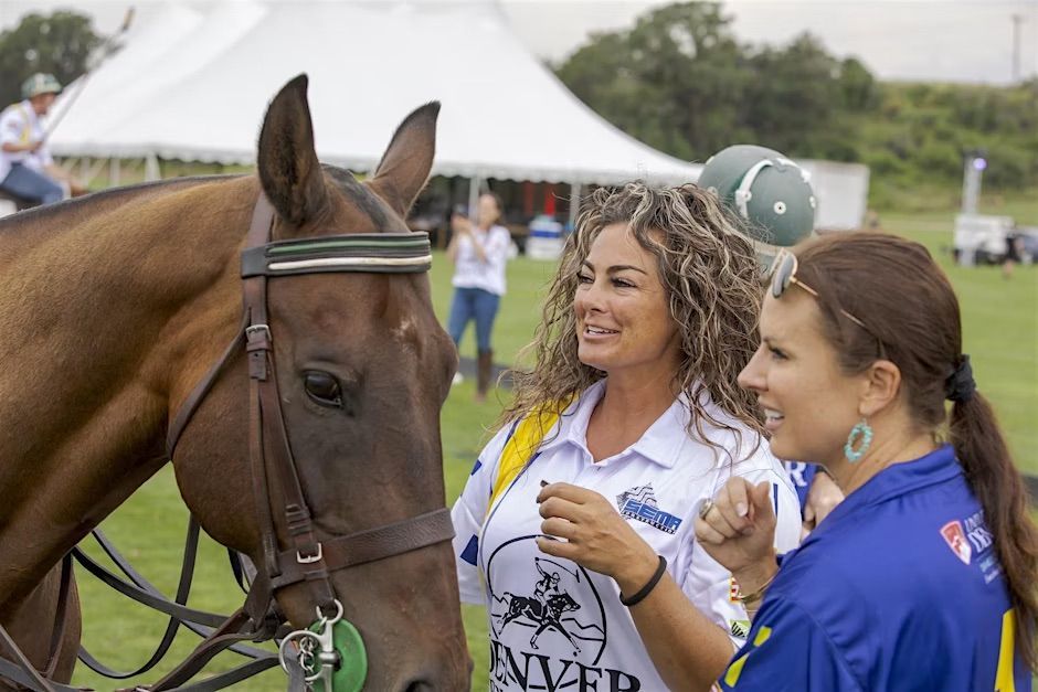 Woman petting a horse, talking with another woman at a polo event.