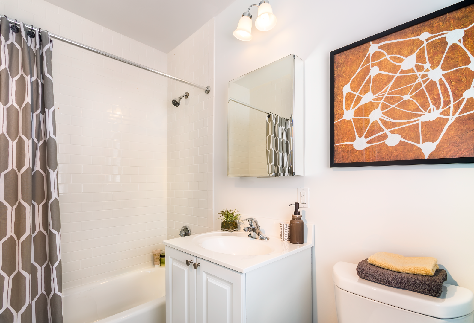 A bathroom with a sink , toilet , shower and a picture on the wall.