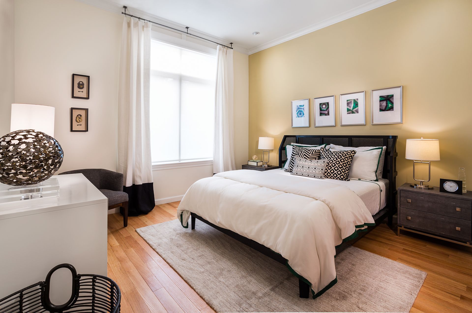Bedroom with bed, nightstands, rug, window, and artwork. Warm-toned walls and wood floors.