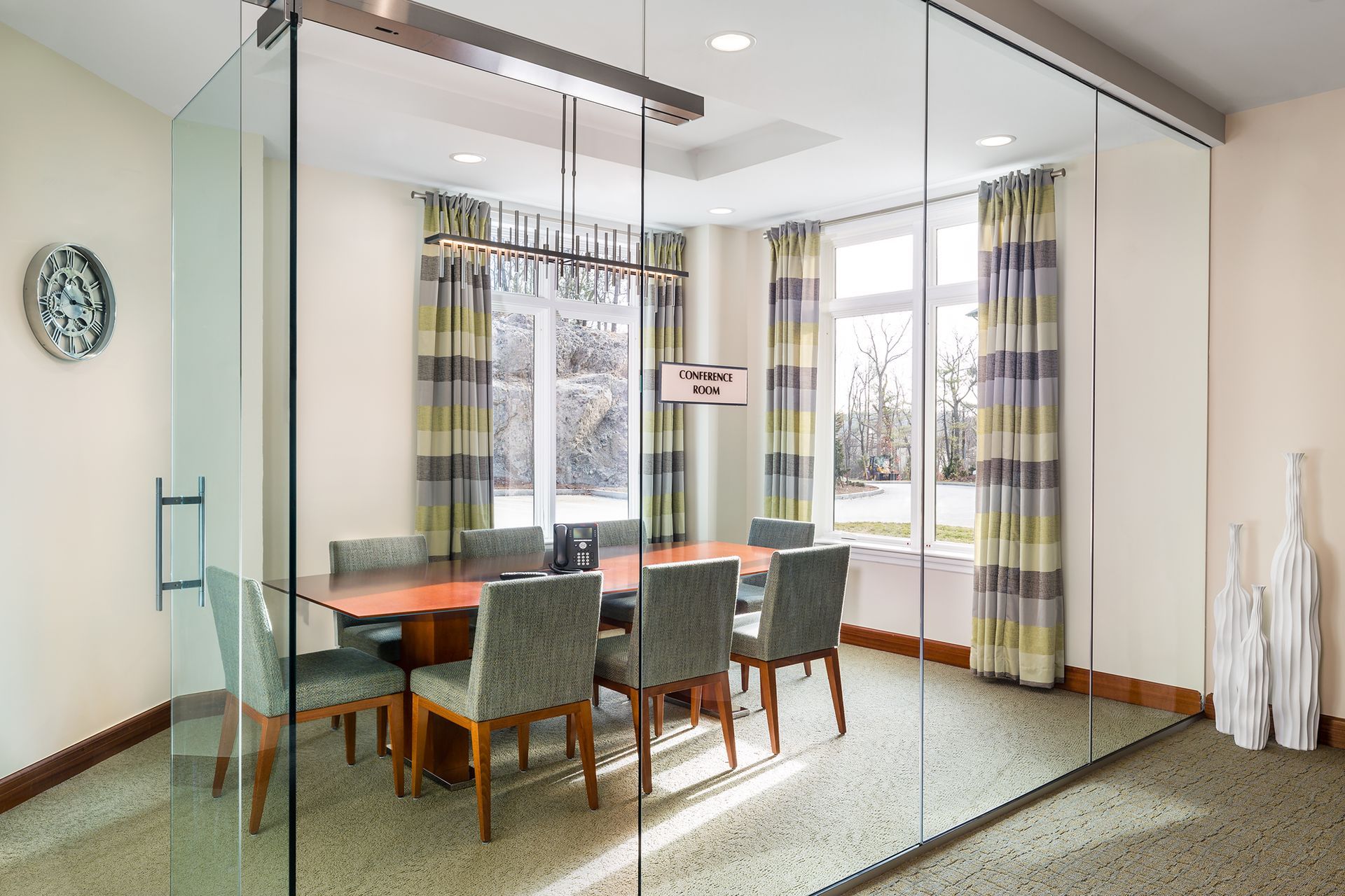 Glass-walled meeting room with table, chairs, windows, and decorative items.