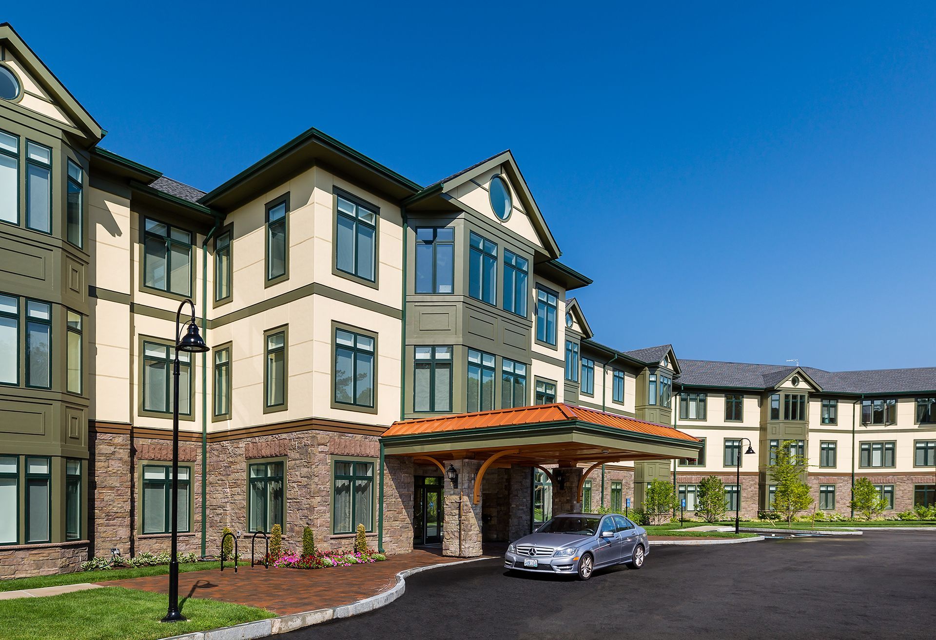 Exterior of a multi-story building with a covered entrance; car parked at the curb under a blue sky.