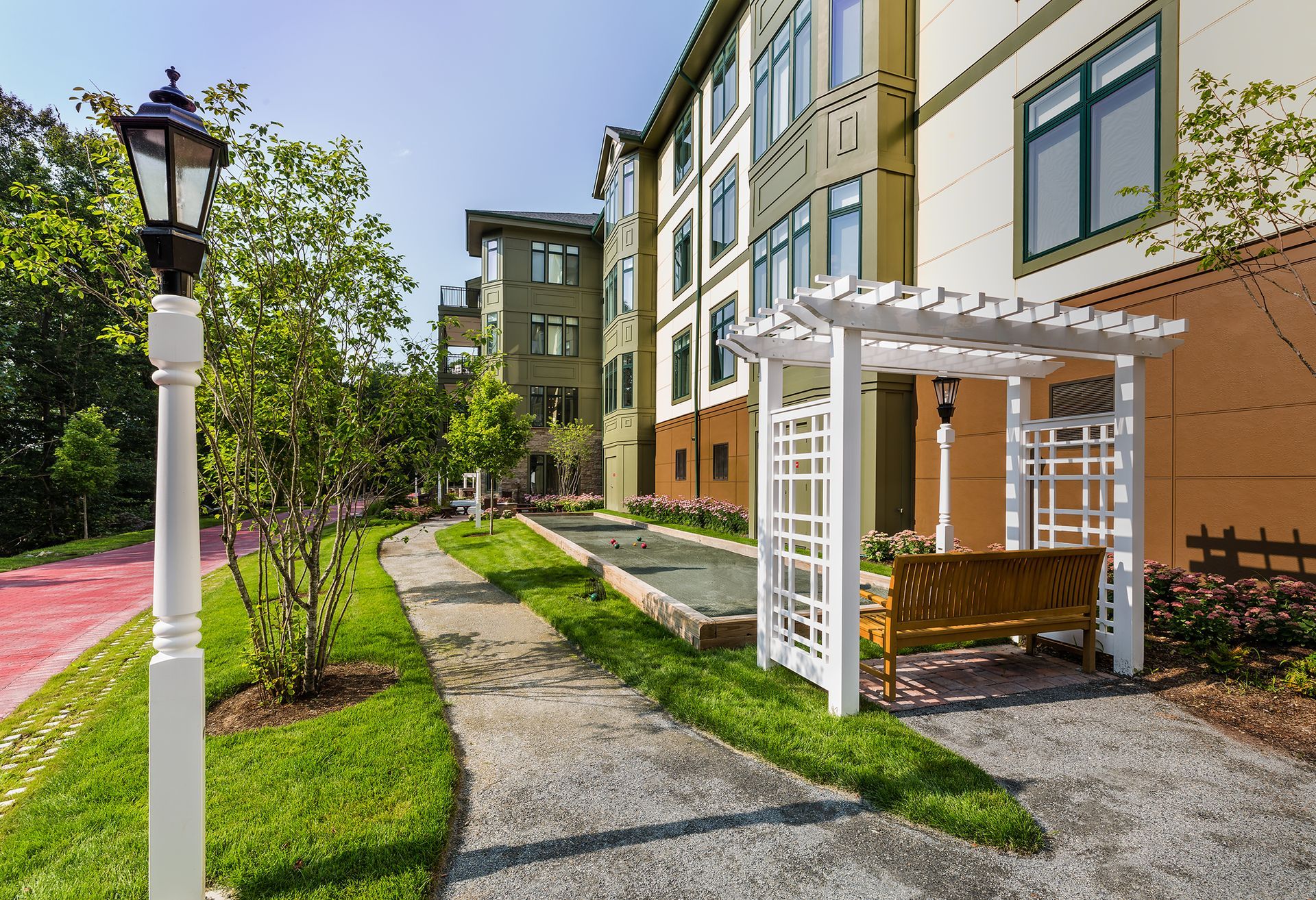 A pathway with a white arbor, bench, and streetlamp in front of a multi-story building.
