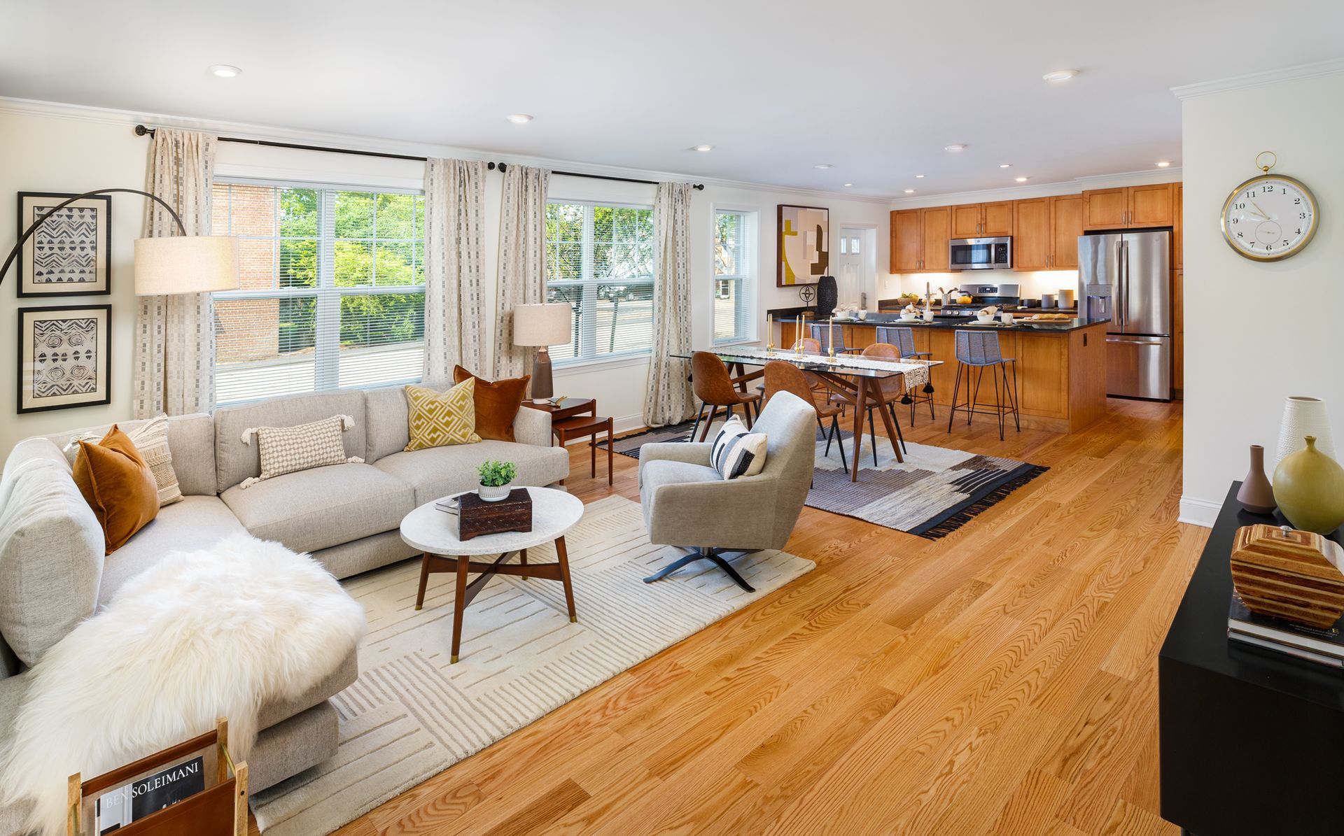Open-concept living room with a sectional sofa, rug, and kitchen in the background with wood floors.