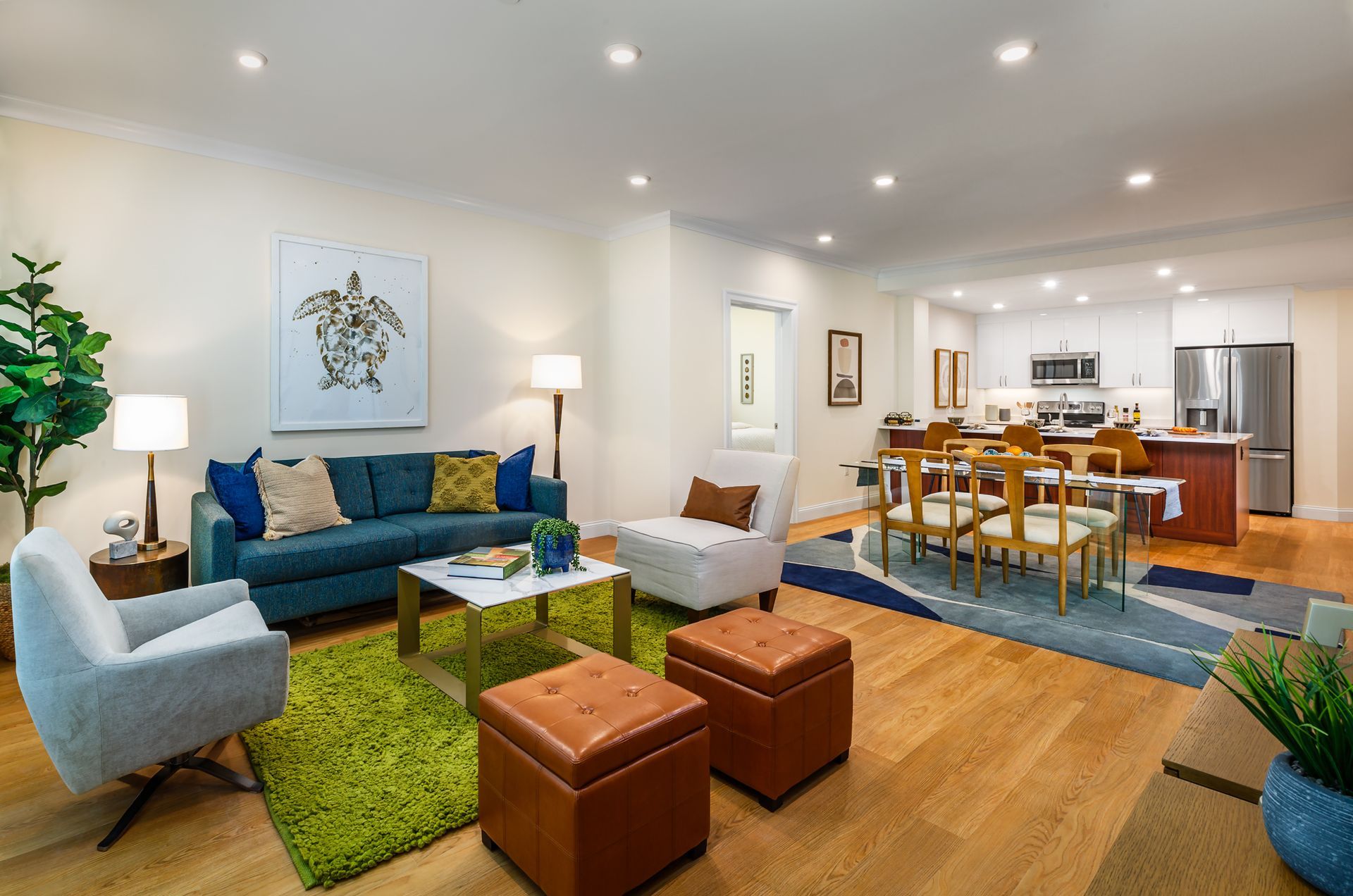 Open-concept living space with teal sofa, green rug, wooden floors, and kitchen in the background.