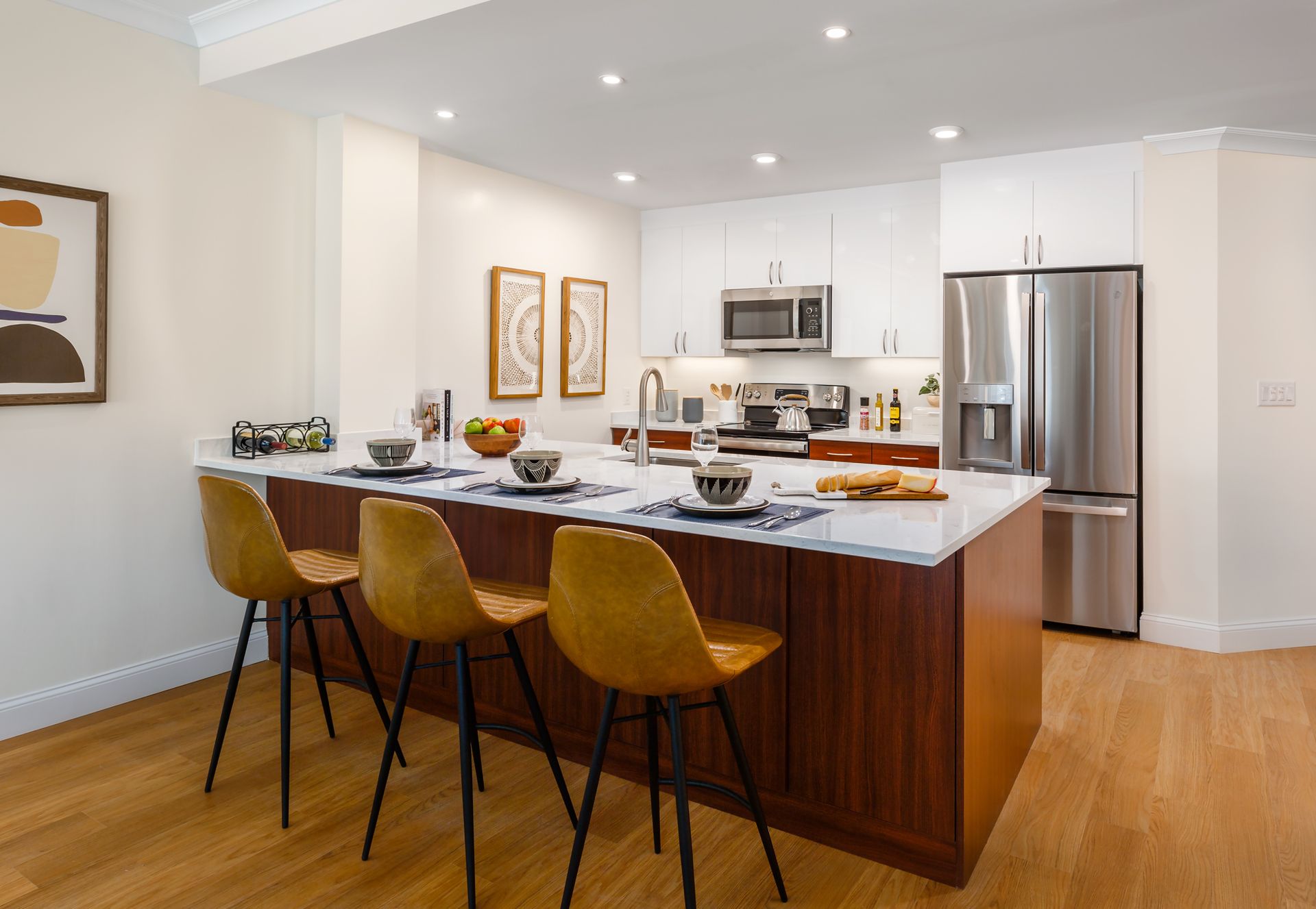 Modern kitchen with wood island, white cabinets, stainless steel appliances, and three bar stools.