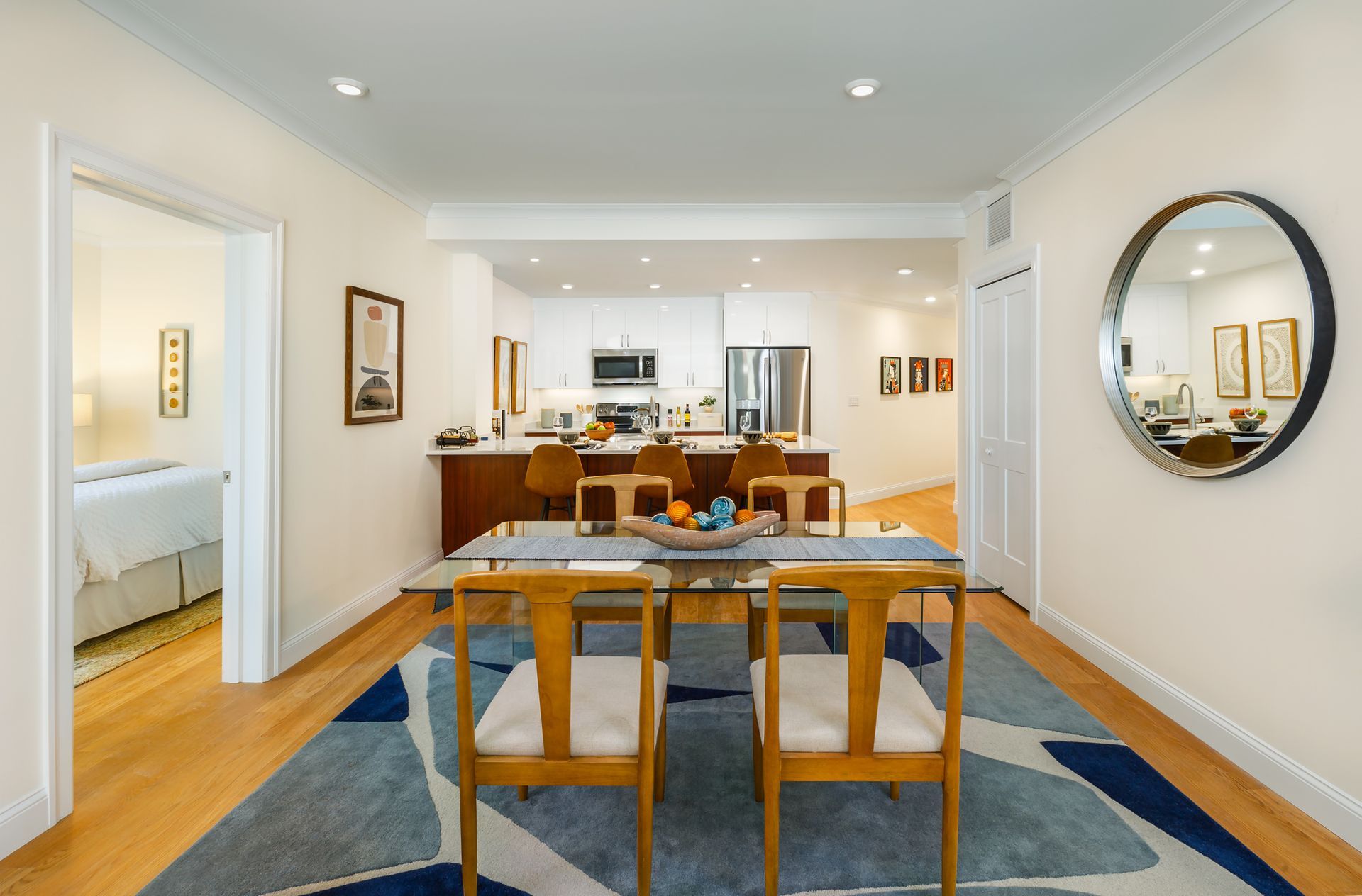 Dining room with table, chairs, blue rug, and open kitchen view.