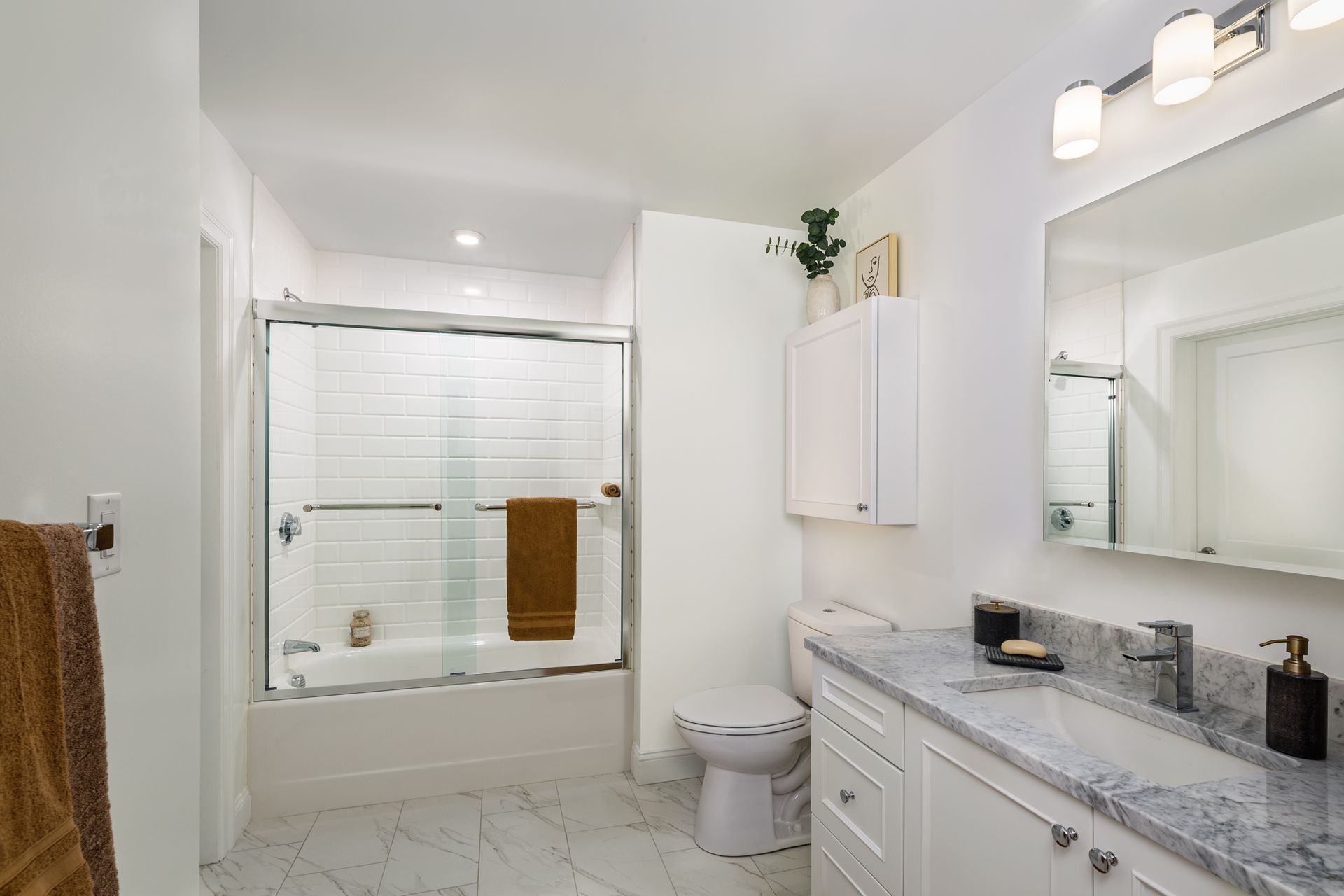 White bathroom with a shower, vanity, and toilet. Framed artwork and towels add color.