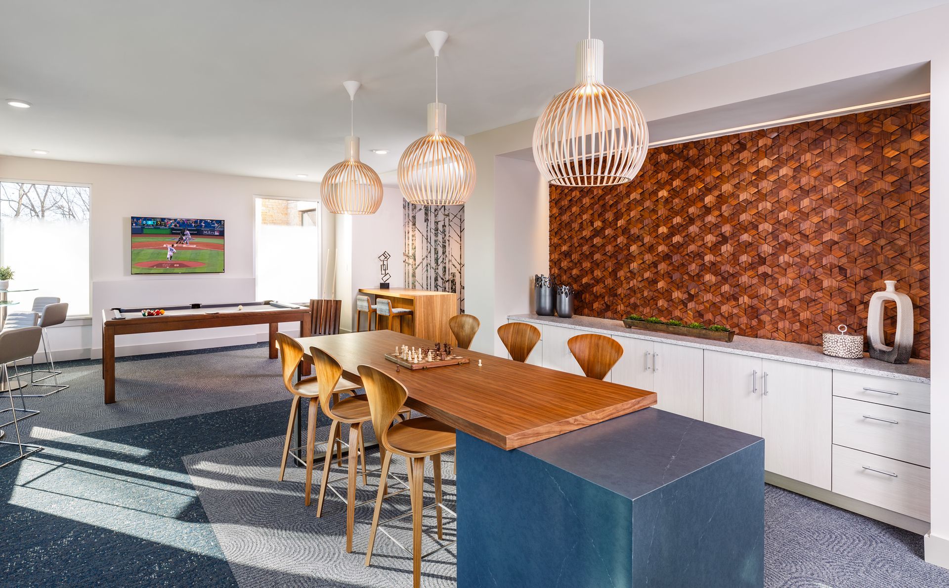 Lounge area with pool table, bar seating, and textured wall. Blue and white speckled floor, pendant lights.