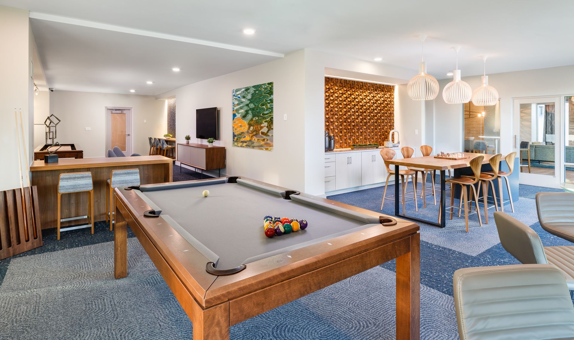 Game room with pool table, bar, dining area, and seating. Blue patterned carpet, neutral walls, and natural wood accents.