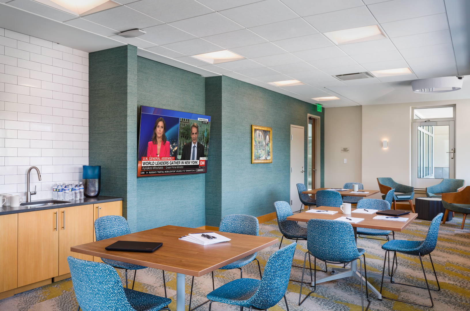 A room with tables and chairs and a television on the wall.