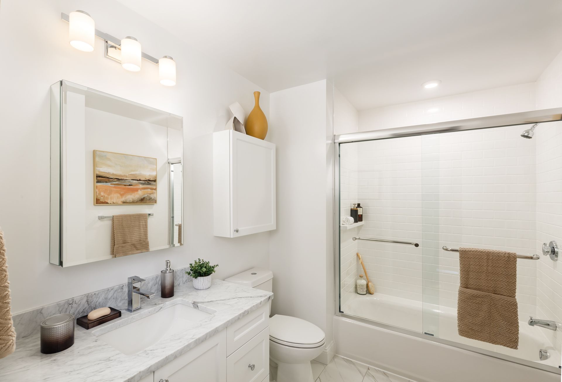 White bathroom with marble countertop, glass shower door, and neutral decor.