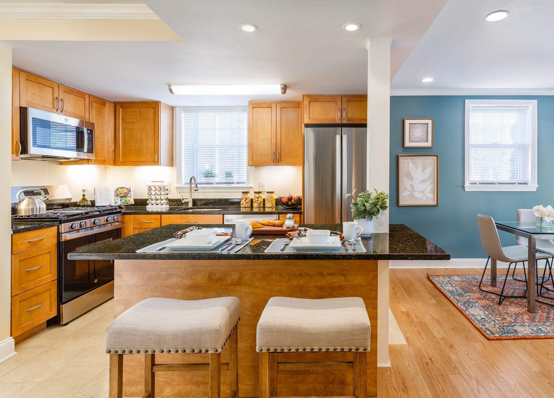 Bright modern kitchen with island, stools, stainless appliances, and adjoining dining area.