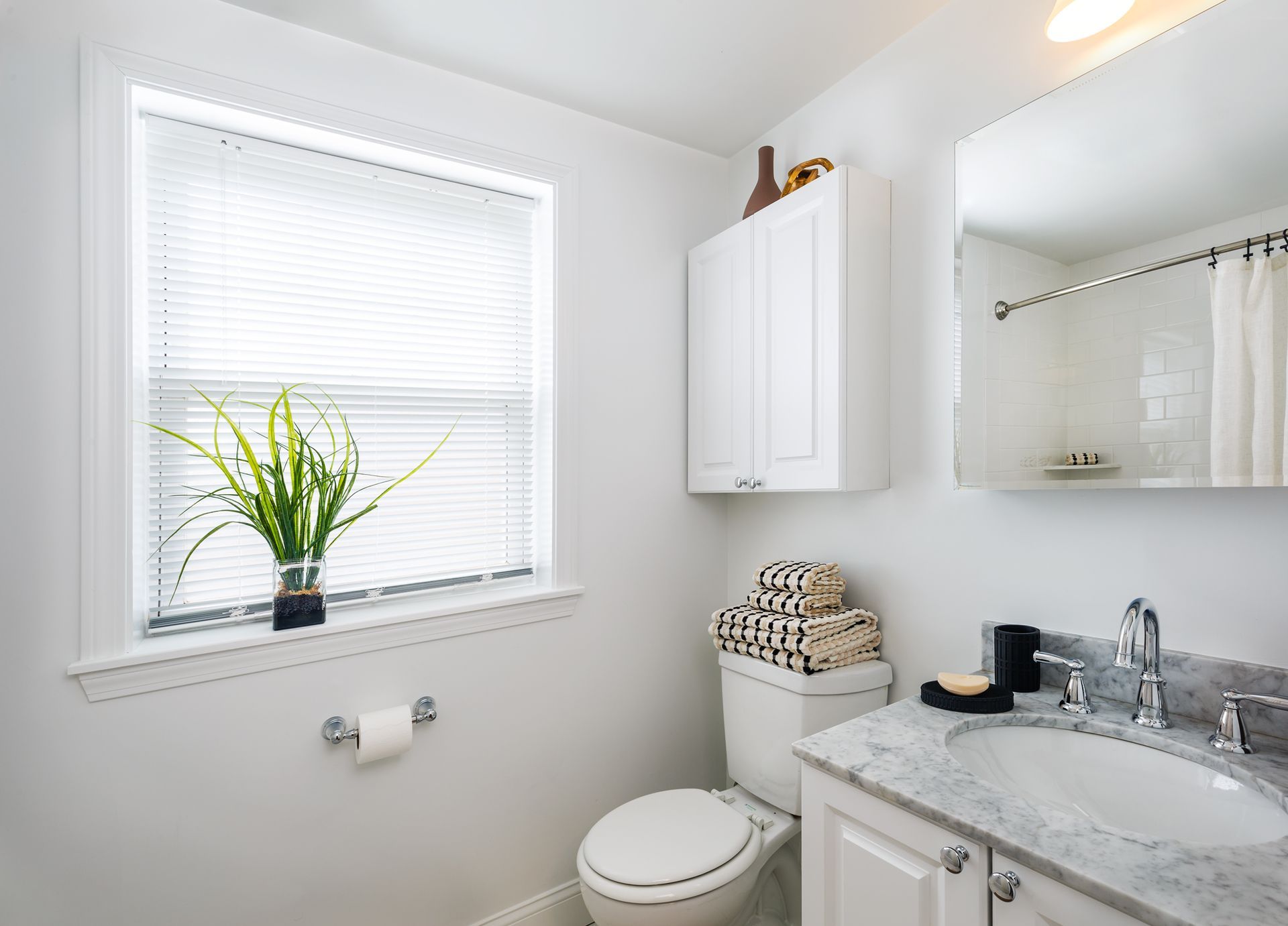 Bright white bathroom with window, vanity, toilet, and potted plant