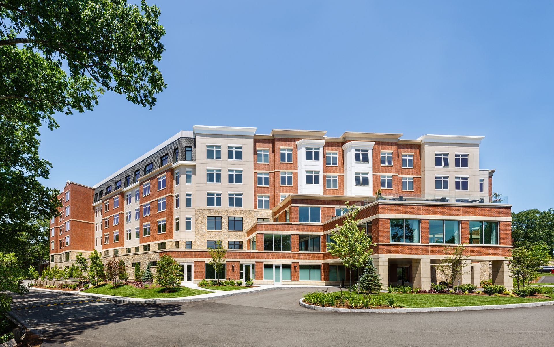 Multi-story brick building with windows under a blue sky, surrounded by trees.