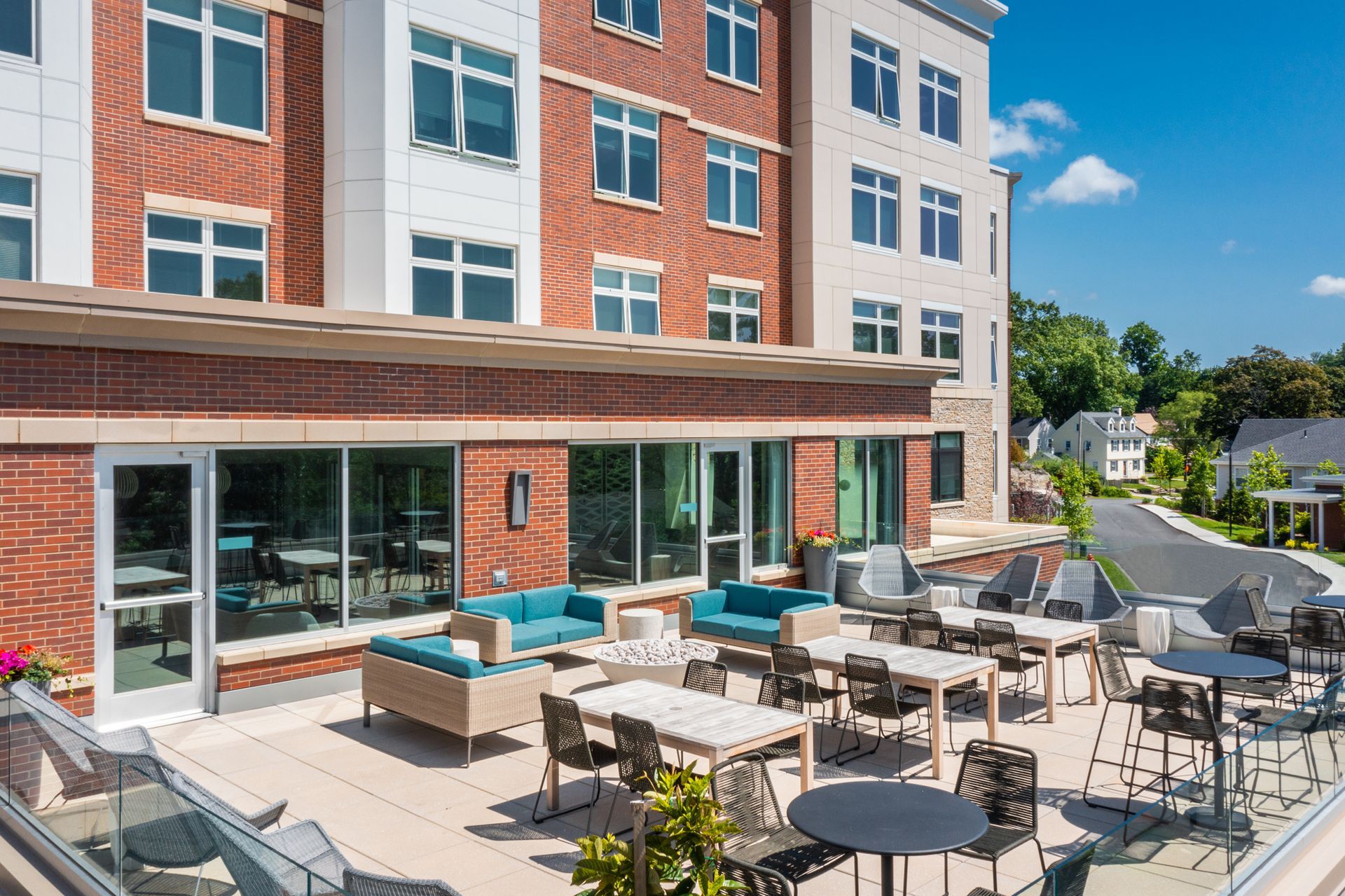 Exterior patio with tables, chairs, and couches. Brick and glass building in the background.