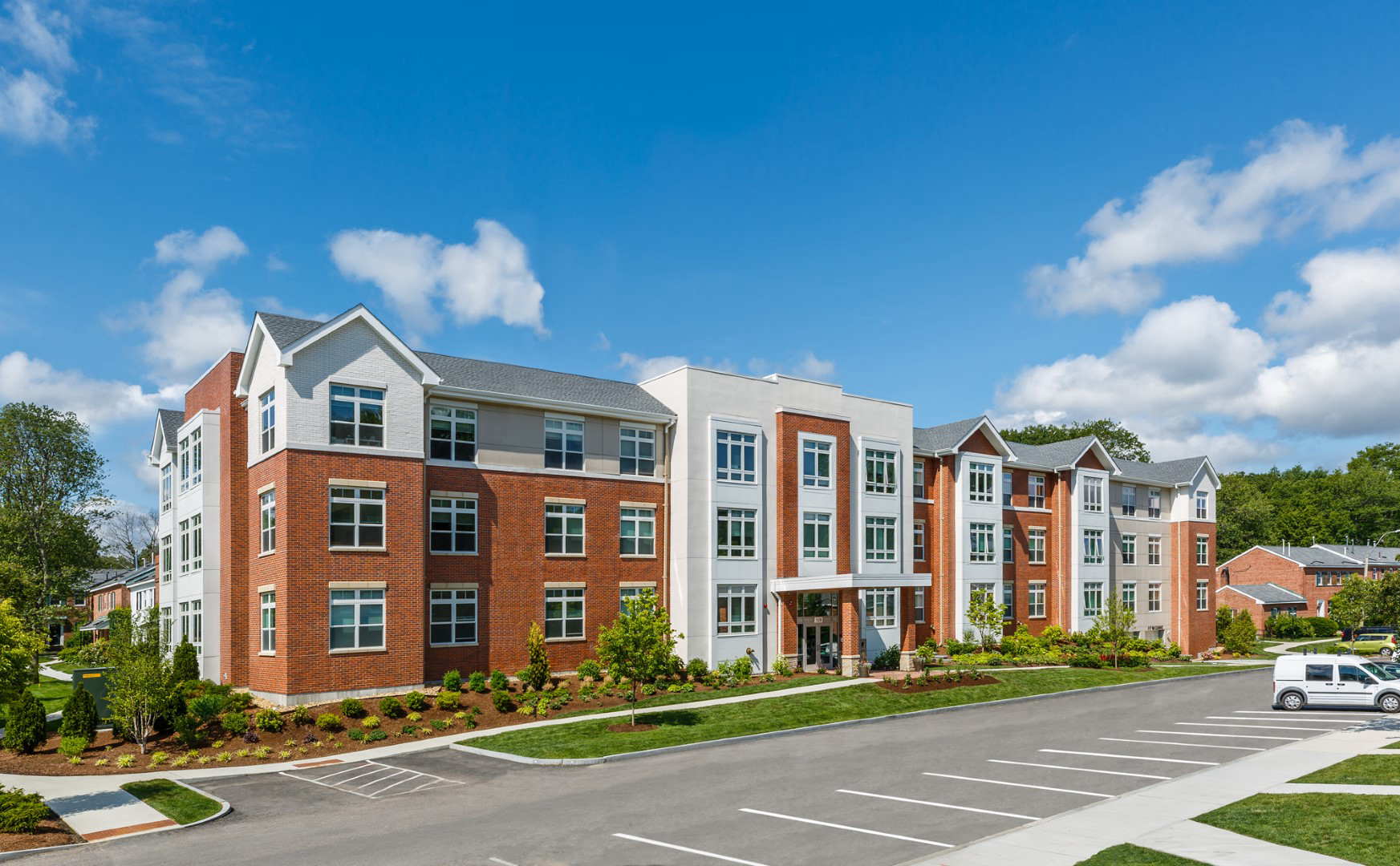 A large brick apartment building with a lot of windows and a parking lot in front of it.