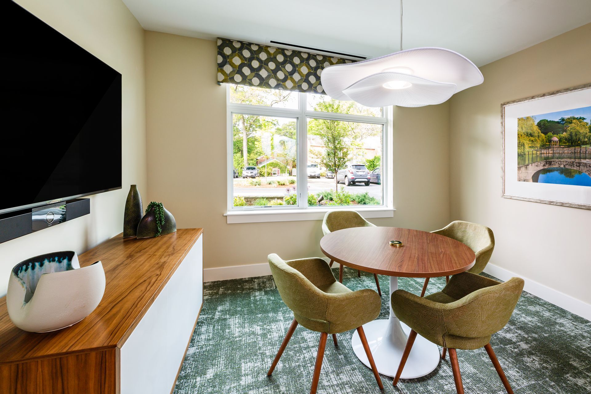 Room with a round table and chairs, a large TV, and a window overlooking an outdoor area.