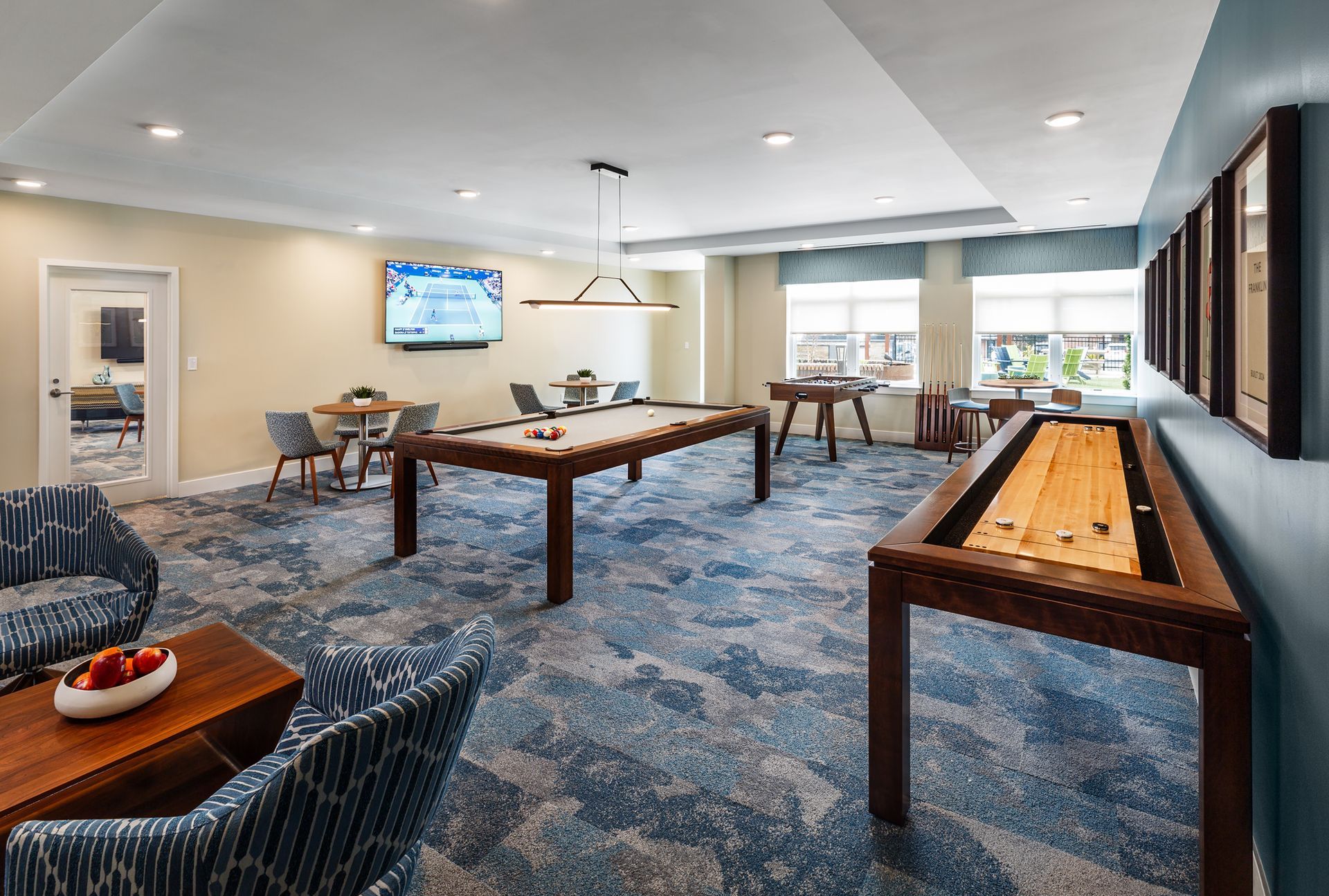 Game room: pool table, shuffleboard, blue patterned carpet, chairs, TV, and large windows.