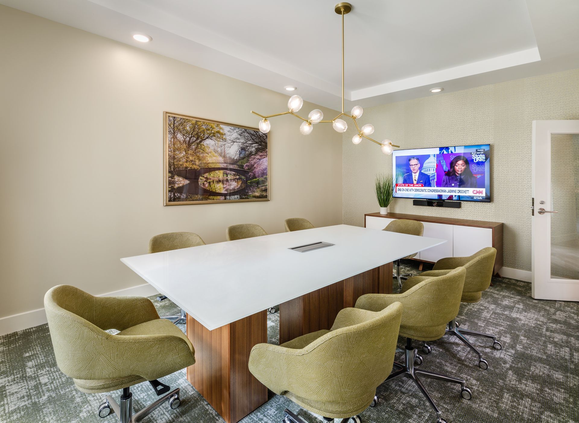 Conference room with white table, gold chairs, art, TV, and light fixture.