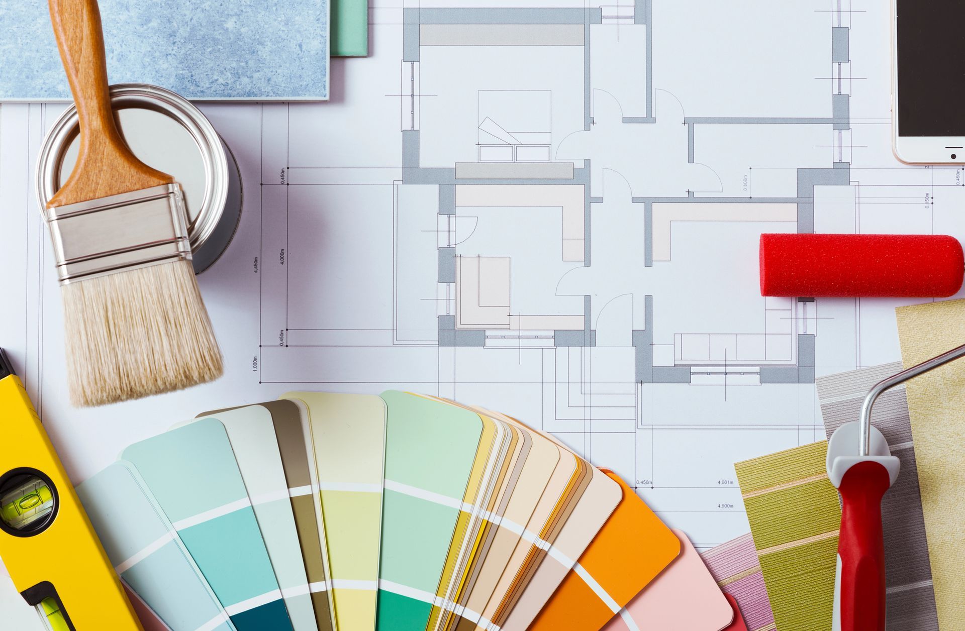Materiali per la pittura e campioni di colore su un progetto, con una livella e un cellulare.