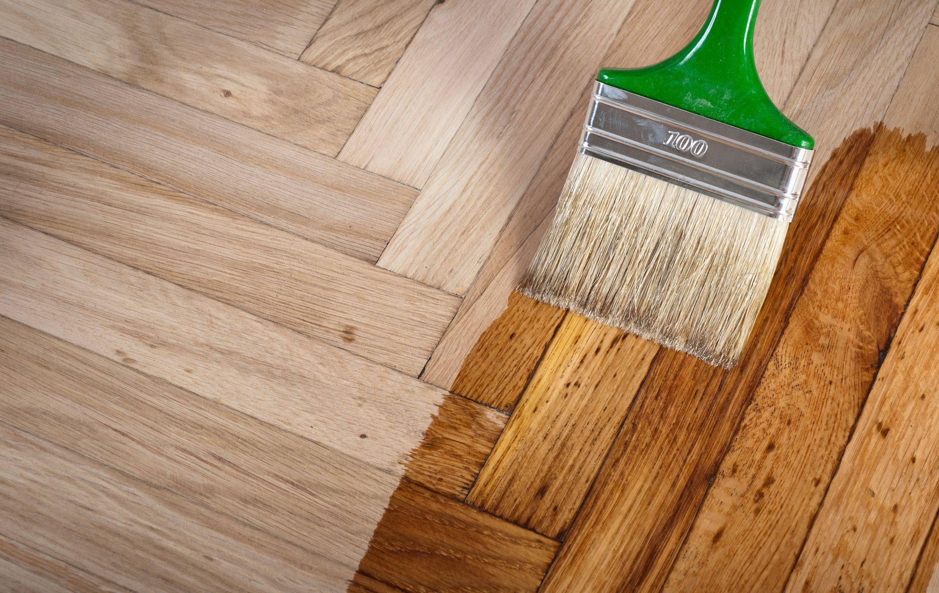 Pennello che applica una tinta marrone su un pavimento in parquet di legno grezzo.