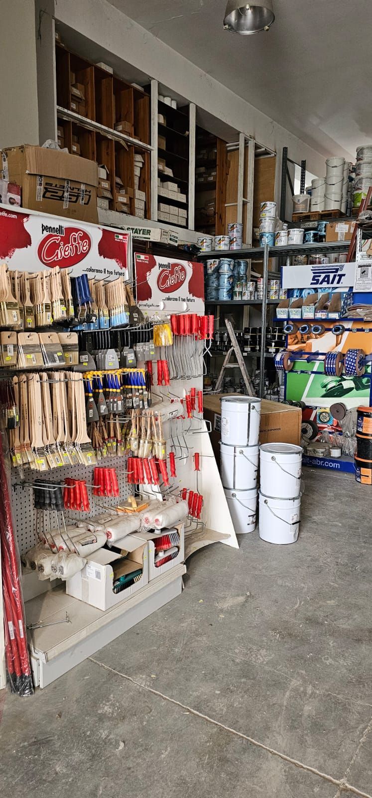 All'interno di un negozio di vernici, scaffali pieni di colori, pennelli e altri materiali. Esposizione di pennelli in primo piano.