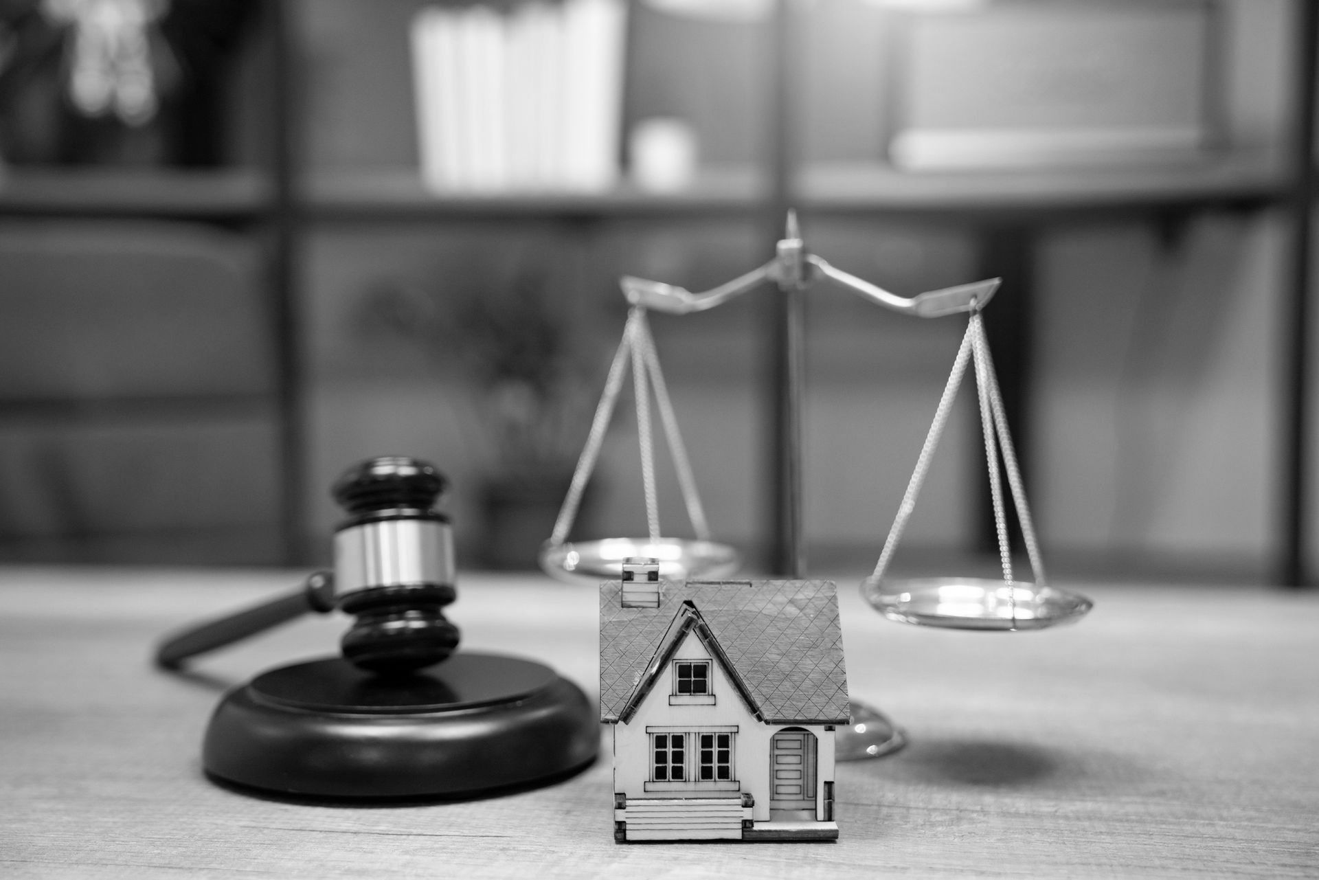 A wooden house is sitting next to a wooden gavel and scales of justice. A wooden house is sitting next to a wooden gavel and scales of justice.