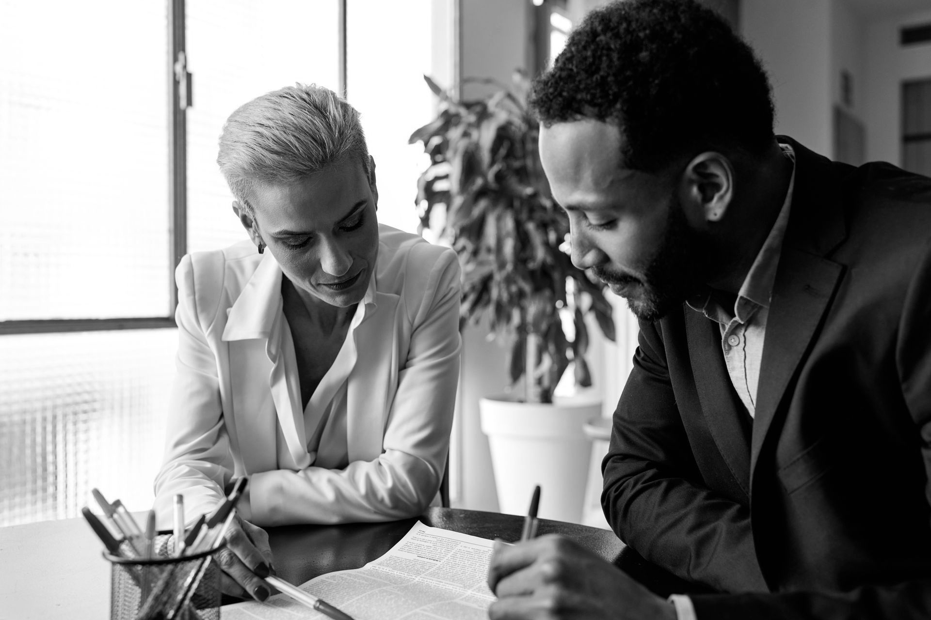 A man and a woman are sitting at a table looking at a book.