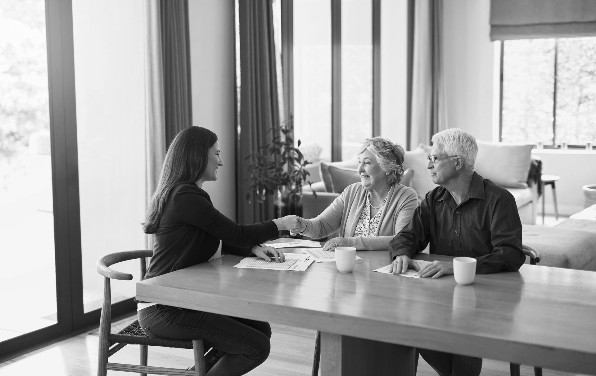 A woman is shaking hands with an elderly couple while sitting at a table.