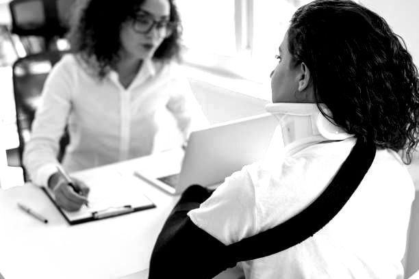 A woman with a broken arm is sitting at a desk talking to a doctor.
