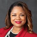 A woman wearing a red jacket and pearls is smiling for the camera.