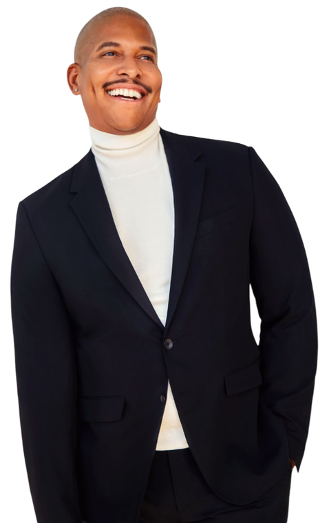 A man in a suit and white turtleneck is smiling.