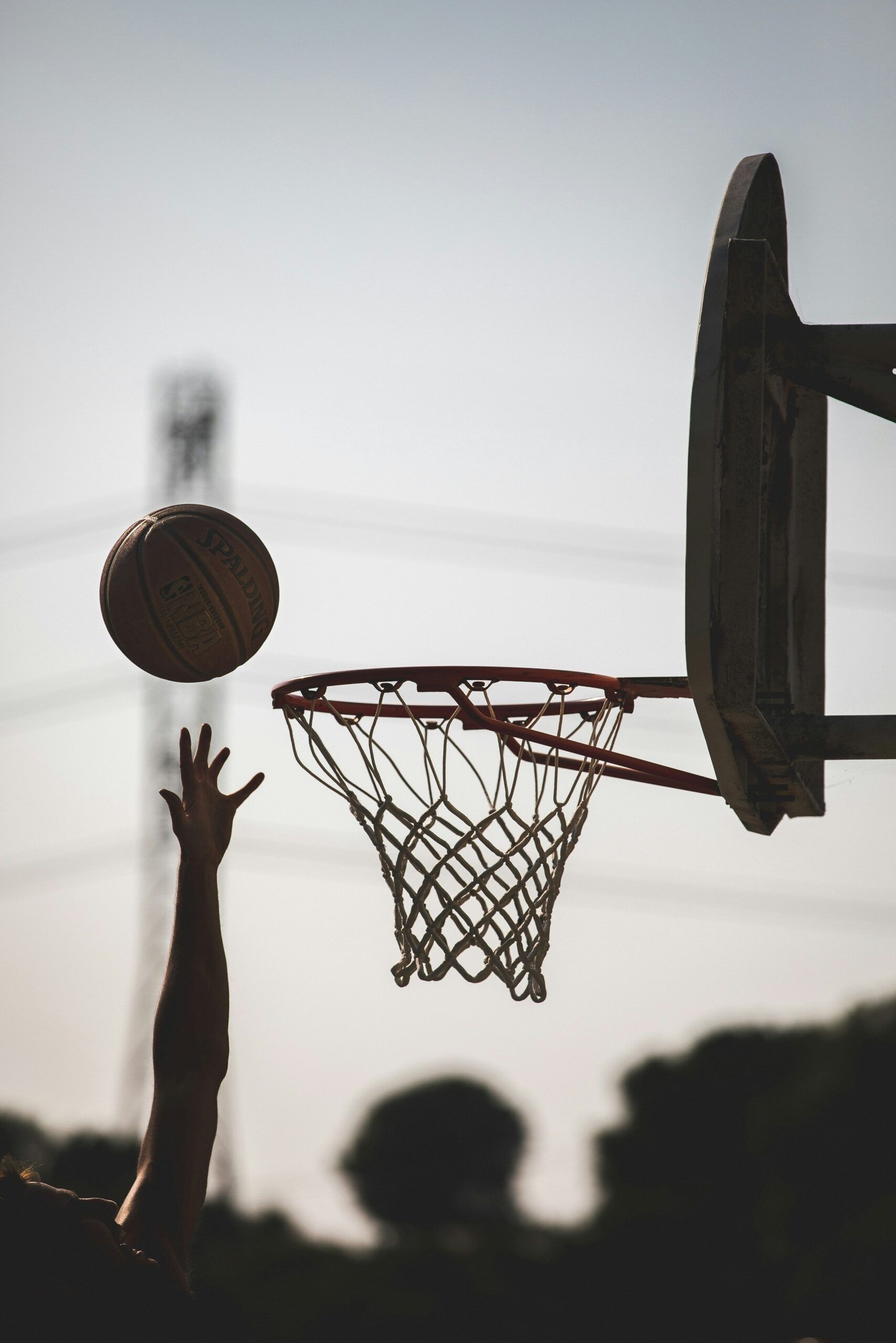 Silhouette of a hand reaching for a basketball near a hoop at dusk