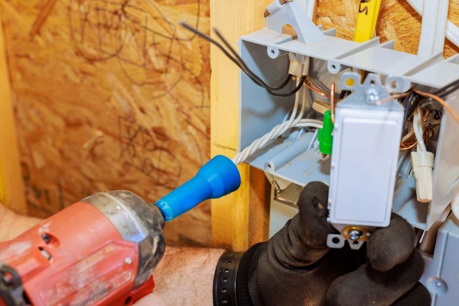 A person is installing a light switch with a power drill. Wires and electrical box are visible.